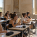 Studenti seduti in un’aula scolastica con finestre aperte e ventilatori accesi.