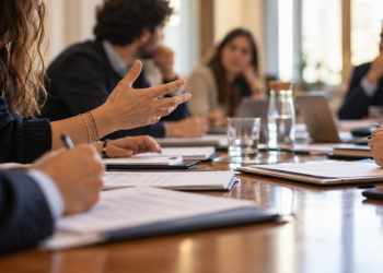 Docenti e giovani rappresentanti si confrontano intorno a un tavolo in una sala riunioni universitaria.