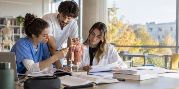 Tre laureati delle professioni sanitarie studiano insieme in un’aula universitaria