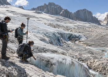Ricercatori universitari misurano il ritiro di un ghiacciaio alpino tra ghiaccio e rocce esposte.