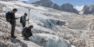 Ricercatori universitari misurano il ritiro di un ghiacciaio alpino tra ghiaccio e rocce esposte.