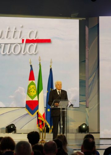 Sergio Mattarella interviene da un leggio trasparente accanto alle bandiere italiana ed europea.