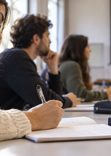 Una studentessa prende appunti durante una lezione universitaria con altri partecipanti