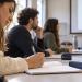 Una studentessa prende appunti durante una lezione universitaria con altri partecipanti