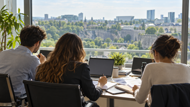 Tre giovani di spalle lavorano su documenti e computer in un ufficio luminoso.