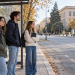 Tre studenti universitari con zaini e quaderni in attesa alla fermata di un autobus.